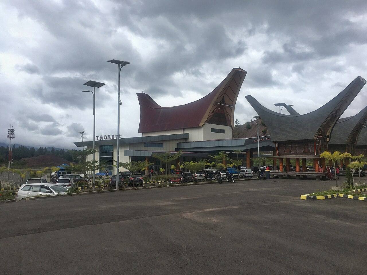 Toraja Airport terminal with curved roofs and TORAJA lettering beside the parking area