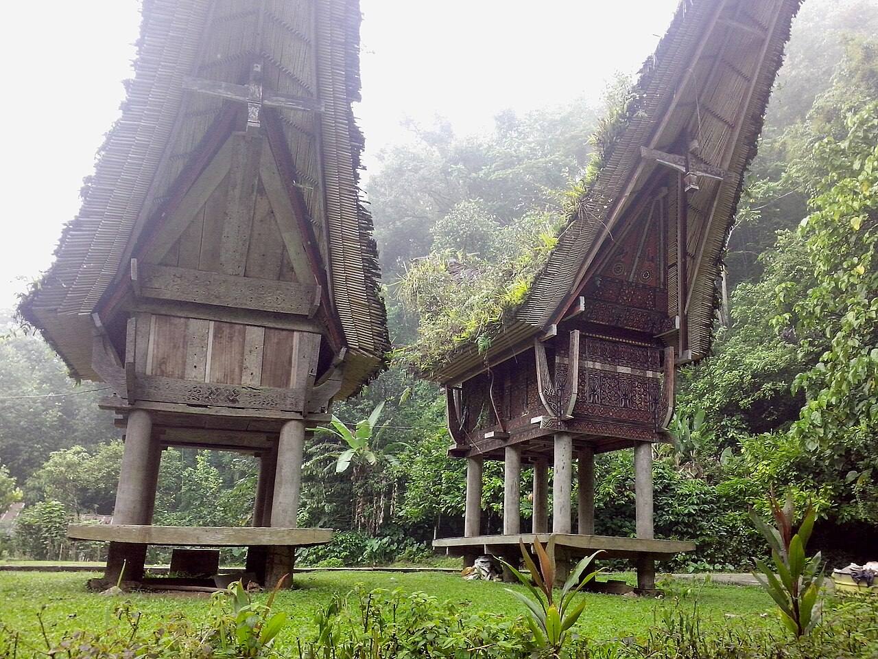 Raised timber rice barns beneath curved roofs at Buntu Pune