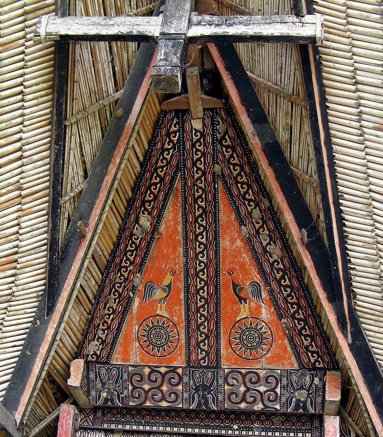 Painted roosters and geometric carving beneath a tongkonan roof at Kete Kesu