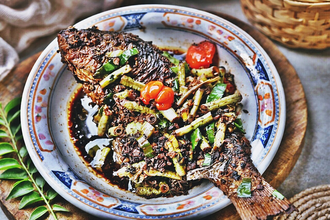 Whole fish in dark pamarrasan sauce with chopped vegetables on a plate