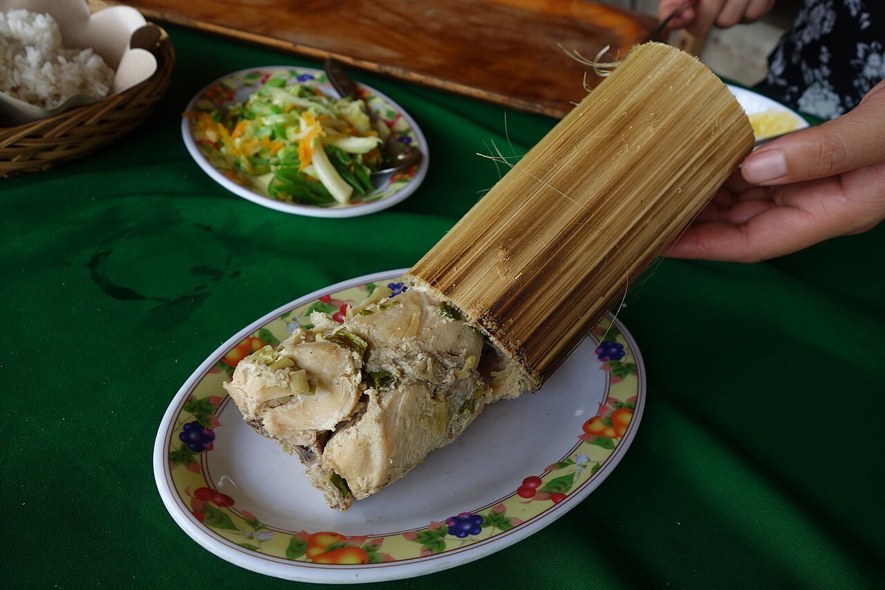 Chicken pa’piong being served from a split bamboo tube onto a plate